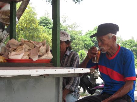An old man drinking tea at a warung